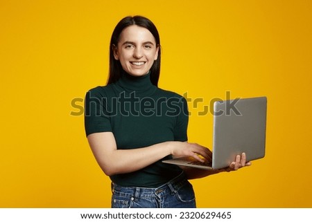 Portrait of a happy caucasian student girl study on laptop computer isolated over yellow background.