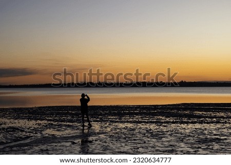 silhouette of a person taking pictures on the beach at sunset