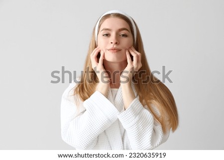 Young woman doing face building exercise on light background