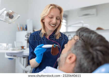 Close up view of man undergoing laser tooth whitening treatment to remove stains and discoloration. Bleaching of the teeth at dentist clinic. Royalty-Free Stock Photo #2320640611