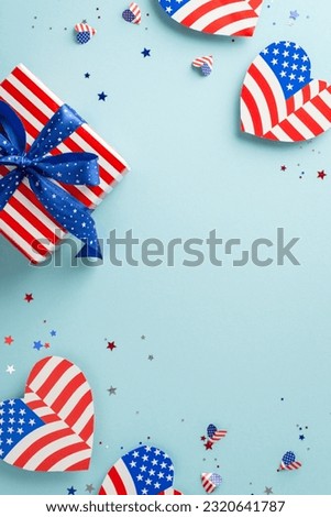 Celebrating Independence Day in USA. Vertical top view of symbolic adornments like hearts with American flag design, confetti, thematic gift box, pastel blue surface with empty space for text or promo Royalty-Free Stock Photo #2320641787
