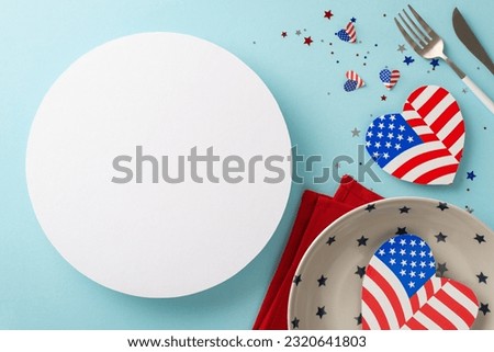 Make arrangements for Independence Day USA with unique table setting. Top view of plate, utensils, napkin, hearts with American flag, confetti on pastel blue backdrop, offering circle for text or ad