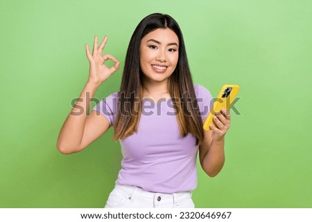 Photo of lovely young vietnamese chinese lady show okey sign gadget dressed stylish violet garment isolated on green color background