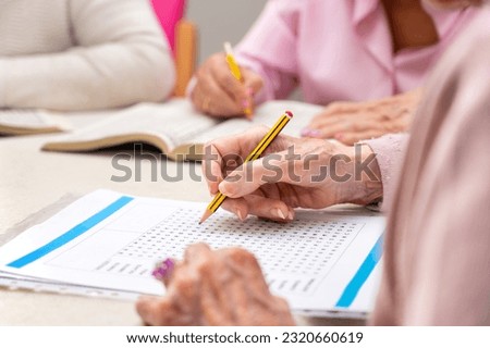 Hands of senior people solving together a word search quiz at nursing home. High quality photo