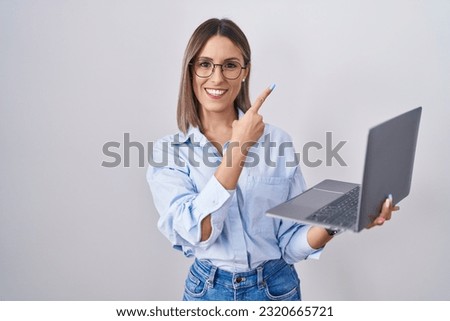 Young woman working using computer laptop cheerful with a smile on face pointing with hand and finger up to the side with happy and natural expression 