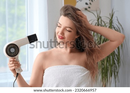 Pretty young woman with hair dryer in bathroom Royalty-Free Stock Photo #2320666957