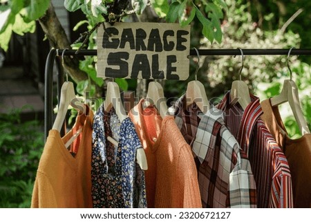 Garage sale, clothes for sale hanging on hanger outdoors.