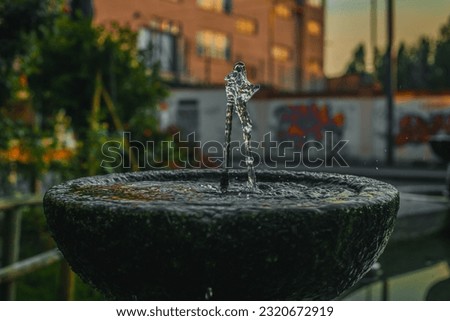 A jet of a street drinking fountain in Milan, Italy. Drinking fountain in a stone bowl outdoors. Close-up photo. Full frame.