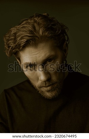 Psychological picture. Art portrait in a dark key of a handsome forty-year-old man with curly hair, dressed in a black pullover, who looks directly and thoughtfully into the camera. People, emotions.
