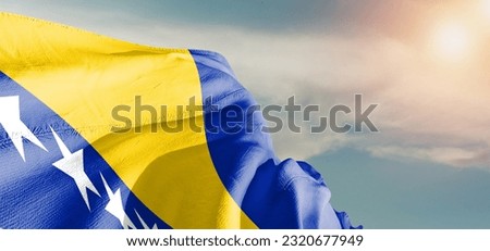 Bosnia and Herzegovina national flag cloth fabric waving on beautiful grey sky Background.