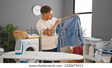 Young man holding denim shirt ironing at laundry room