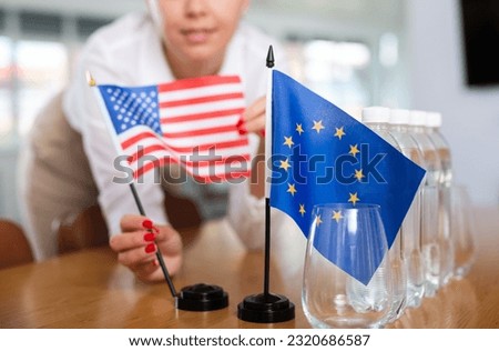..Young woman in business clothes puts flags of USA and European Union on negotiating table in office