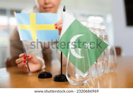 Young woman in business clothes puts flags of Sweden and Pakistan on negotiating table in office