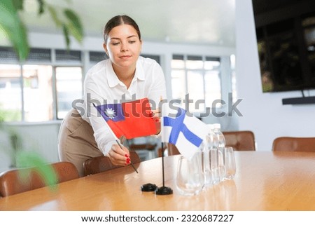 Young woman in business clothes puts flags of Taiwan and Finland on negotiating table in office