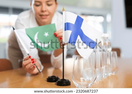 Young woman in business clothes puts flags of Pakistan and Finland on negotiating table in office..