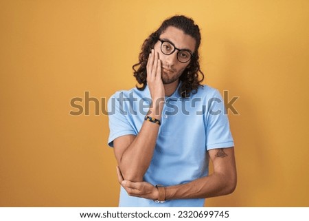 Young hispanic man standing over yellow background thinking looking tired and bored with depression problems with crossed arms. 