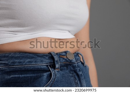 Overweight woman in tight shirt and jeans on grey background, closeup. Space for text Royalty-Free Stock Photo #2320699975