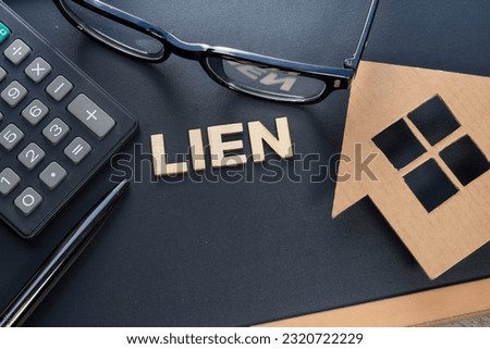 Concept on property financing. The word LIEN made from wood on the black background. A house model, eyeglasses, pen and calculator.