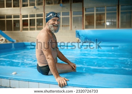 Relaxed senior man in swimming hat and goggles on head sitting at poolside