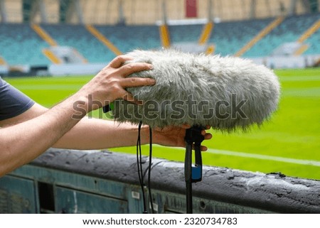 Preparations for the television channel's live broadcast of a football match. The sound technician is placing microphones along the edges of the football field.