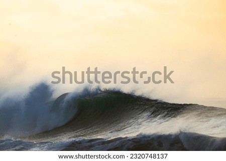huge shore break wave crashing on the beach at sunset