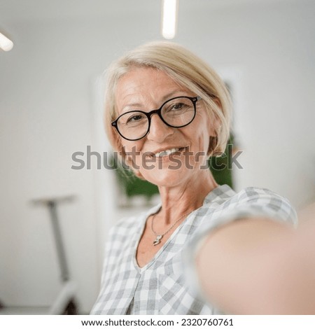 Portrait of one mature blonde caucasian woman with eyeglasses at home happy smile looking to the camera confident wear sweater in bright room user generated content self portrait selfie ugc copy space Royalty-Free Stock Photo #2320760761