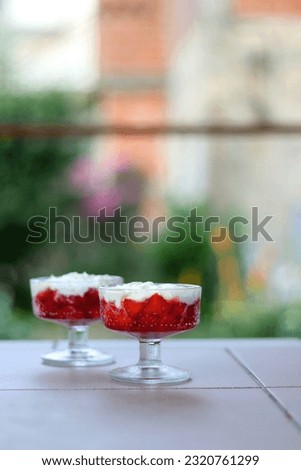 Two bowls of strawberries and whipped cream, served in a garden. Selective focus.