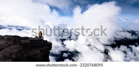  tourist in the mountain sitting on a big rock admiring the landscape with clouds, concept of adventure and outdoor sports.