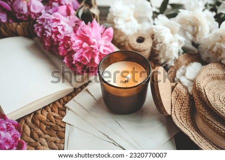 Cozy spring composition, burning candle, peonies and hat.