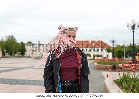 A young beautiful girl with pink dreadlocked hair dances with headphones on a city street.