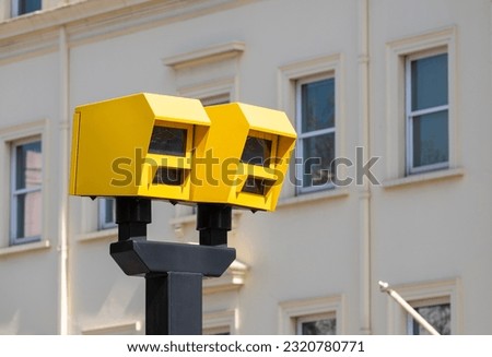 Low angle view of two bright yellow speed safety cameras against an urban background.