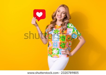 Photo of shiny dreamy woman dressed flower print t-shirt holding heart like card looking empty space isolated yellow color background