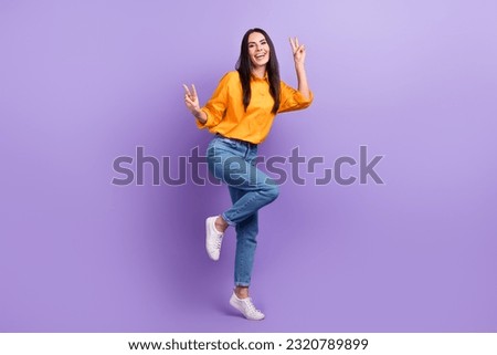 Full length photo of pleasant optimistic girl dressed yellow shirt pants showing v-sign symbol isolated on purple color background