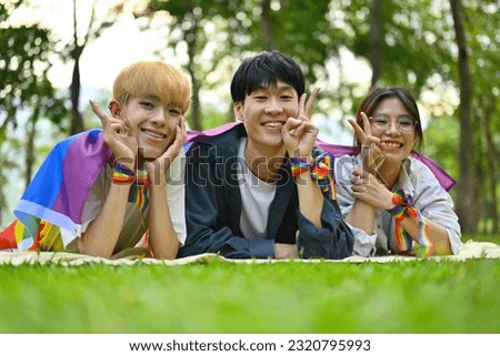 Pictured with a group of LGBT teenagers lying on the lawn, covered with rainbow flags and wearing a rainbow wristband, freedom concept, Celebration Pride month in June.