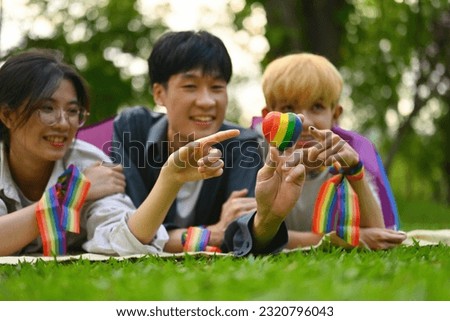 Support the expression of LGBT identity and outdoors concept wit A group of LGBT Asian teenager staring at the Rainbow Heart model while lying on the lawn, Selective focus on Heart model.