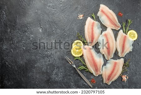 Raw tilapia fish fillet sliced for steak with lemon and spices on a dark background. Long banner format. top view,