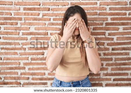 Young brunette woman standing over bricks wall rubbing eyes for fatigue and headache, sleepy and tired expression. vision problem 