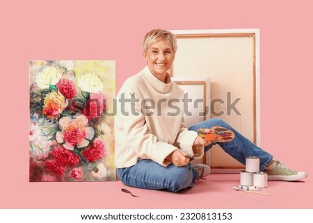 Mature female artist with picture and tools on pink background
