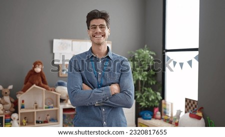 Young hispanic man preschool teacher smiling confident standing with arms crossed gesture at kindergarten Royalty-Free Stock Photo #2320817655