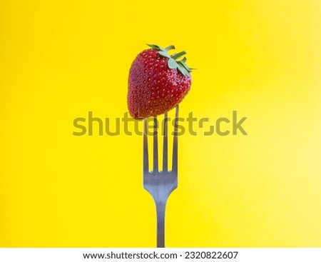 Strawberry stabbed on a silver fork on the yellow background. Close-up.