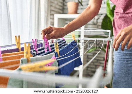 A young Caucasian woman, hanging clothes on a clothesline in front of her home window, embracing household tasks with a positive attitude. Royalty-Free Stock Photo #2320826129