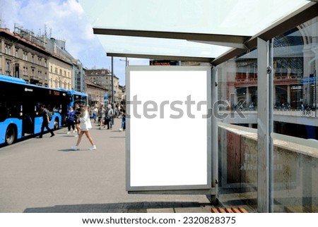 bus shelter with blank ad panel. billboard display. empty white lightbox sign at bus stop. billboard mockup. glass structure. city transit station. urban street. park setting. outdoor advertising.
