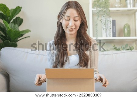 Happy excited, asian young woman, girl customer sitting on sofa at home, opening and unpacking cardboard box carton parcel after buying ordering present, shopping online, delivery service concept. Royalty-Free Stock Photo #2320830309