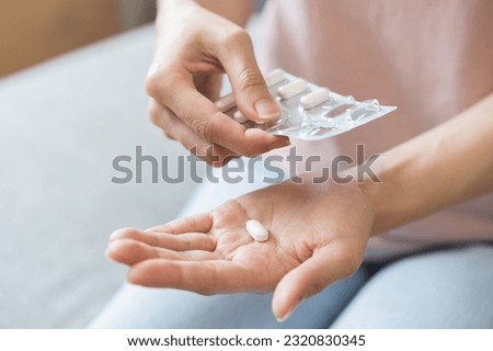 Sick ill asian young woman, girl hand taking tablet pill capsule out from blister pack, painkiller medicine from stomach pain, head ache, pain for treatment, take drug or vitamin at home, health care. Royalty-Free Stock Photo #2320830345