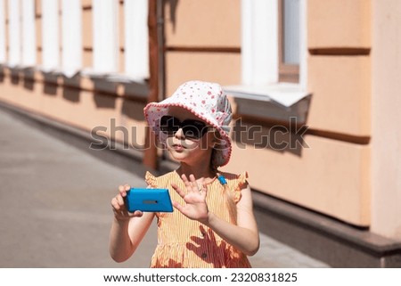 Beautiful little girl in a panama hat takes a photos or shoots a video on the smartphone, travel, blogger.