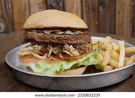 Plant based burger. Not Burger. Closeup view of NotCo hamburger with tomato, lettuce, crispy onion rings and NotCo mayo, in a metal dish on the restaurant wooden table.