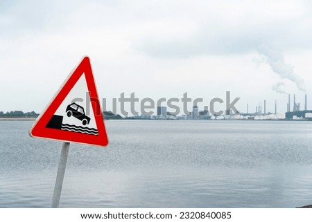 Traffic sign Attention shore on the left in the picture, in the background you can see defocused water and harbor buildings, horizontal 