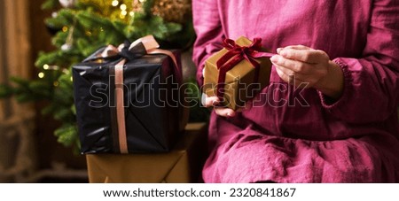 Banner for Christmas with gifts. A woman in a burgundy dress holds gifts with a bow against the background of a Christmas tree.