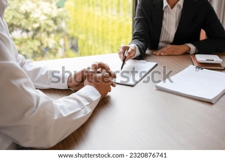 Female real estate agent in suit negotiating about house price, finance, and agreement with buyer or client at desk showing document detail and information before signing contract. 
