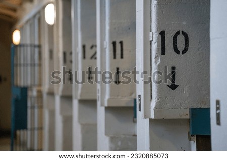 the consecutive numbers ten eleven and twelve painted on sides of concrete columns of prison cells of jail or institutional facility with open door in background horizontal image with room for type 